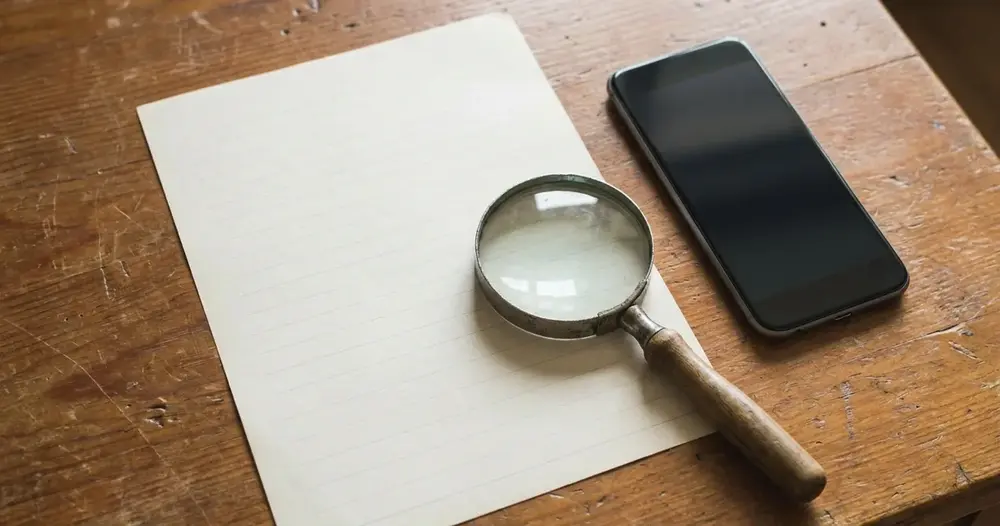 Documento impresso sobre a mesa com lupa e celular para conferir a nota fiscal