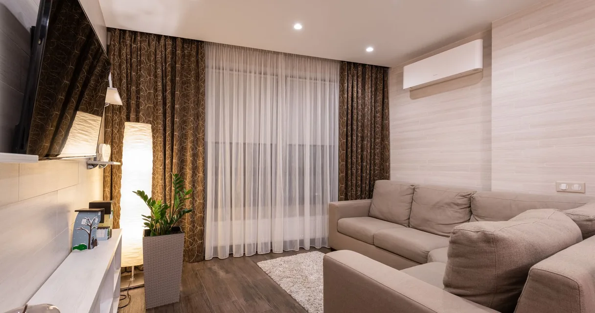 Sala de estar com sofá bege, cortinas e ar condicionado split instalado na parede alta